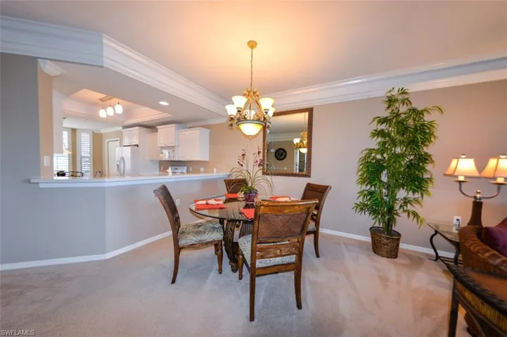 Dining area with a chandelier, ornamental molding, light colored carpet, and a tray ceiling
