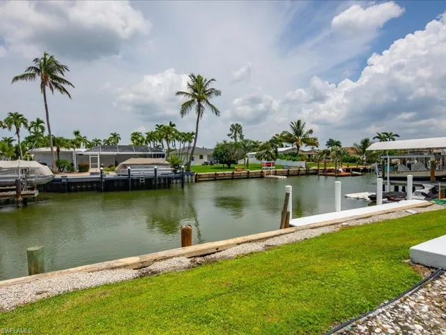 Waterfront canal with multiple boat docks featuring pilings, boat lifts, and mature palm trees