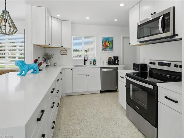 Modern kitchen featuring white cabinetry with matte black hardware, stainless steel appliances, white countertops, and terrazzo flooring