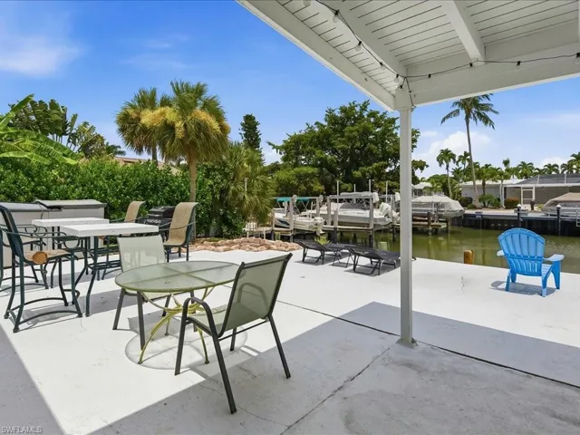 Waterfront patio area with a covered section, concrete flooring, and tropical landscaping