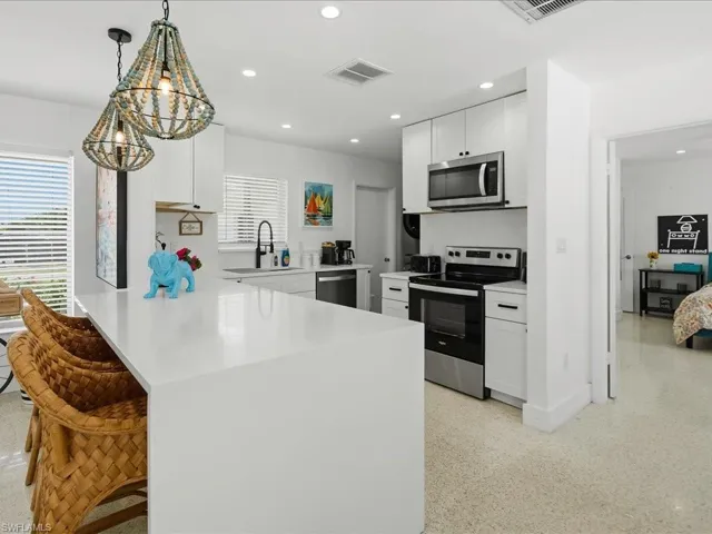 Contemporary kitchen featuring a large waterfall island, white cabinetry, stainless steel appliances, and terrazzo flooring