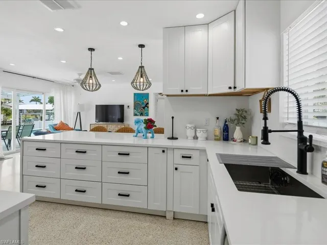 Modern kitchen featuring white shaker cabinetry, an expansive island with storage, light-toned countertops, a black pull-down faucet, and recessed lighting