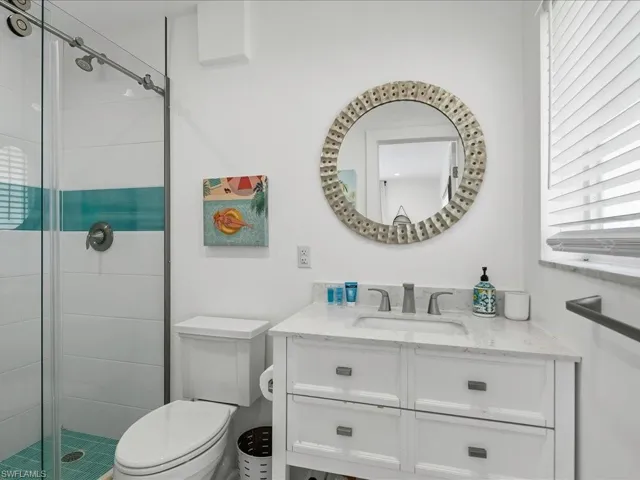 Bathroom featuring a glass-enclosed shower with tile accent band, a single vanity with stone countertop, wood-finish cabinetry, and an ornate circular mirror
