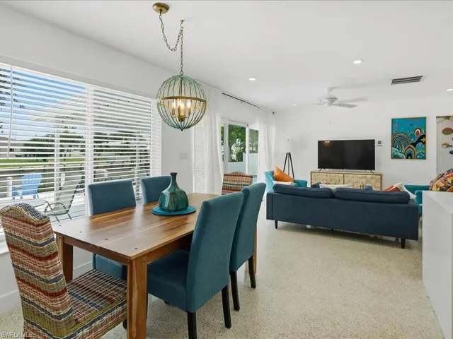 Open-concept living area featuring a dining space with a wood table, a decorative chandelier, and large windows with horizontal blinds