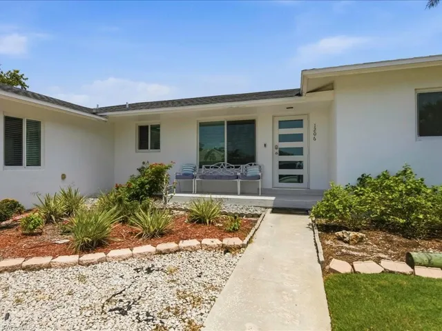 Modern white exterior with a contemporary front door featuring frosted glass panels, a concrete walkway, and a gravel and mulch landscape with various plants