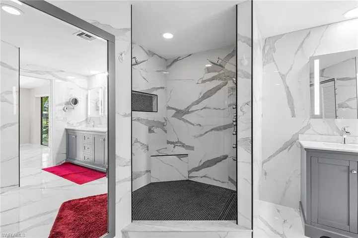 Full bath featuring stone wall, marble tiled floors, two vanities, recessed lighting, and tile walls