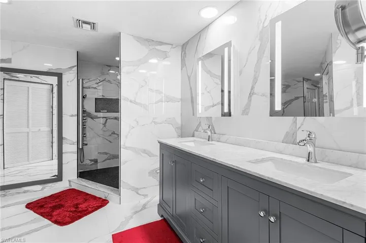 Bathroom featuring stone wall, light marble finish flooring, double vanity, a marble finish shower, and tile walls