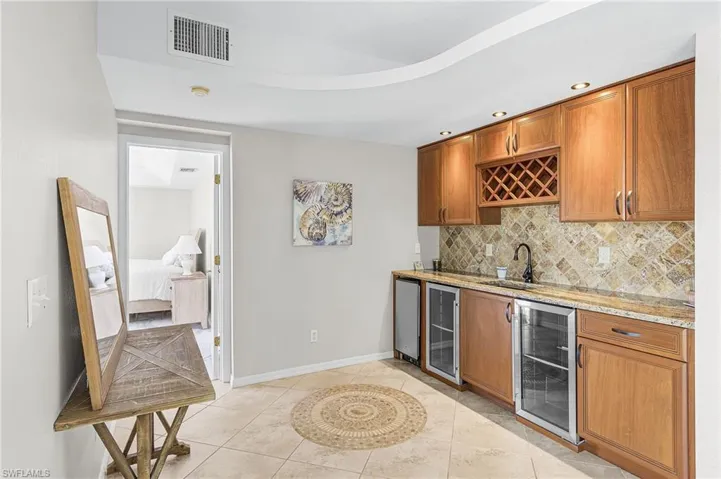 Indoor wet bar featuring light stone countertops, brown cabinetry, beverage cooler, backsplash, and recessed lighting