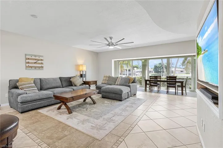 Living room featuring ceiling fan, light tile patterned floors, inlaid floor details, and a textured ceiling