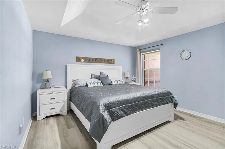 Bedroom with light wood-type flooring, a ceiling fan, and a raised ceiling
