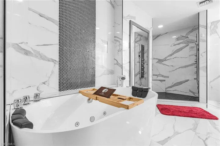 Full bath featuring a tub with jets, a marble finish shower, marble tiled flooring, tile walls, and stone wall