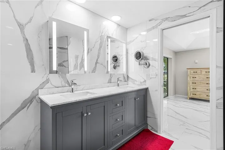 Bathroom featuring marble tiled floors, stone wall, double vanity, recessed lighting, and tile walls