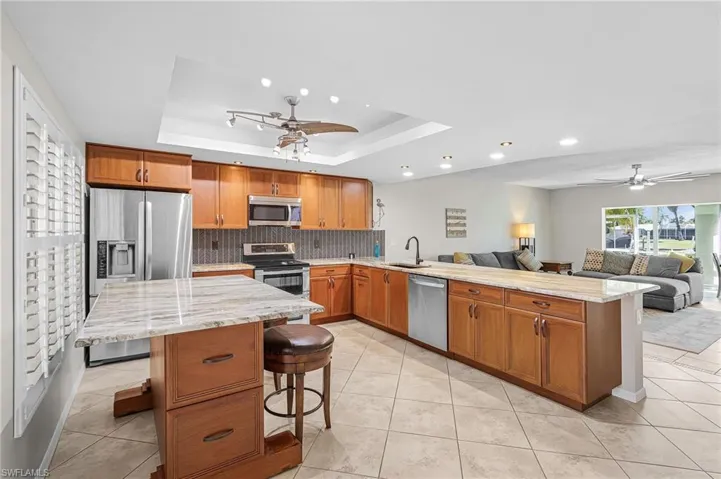 Kitchen featuring a ceiling fan, brown cabinets, open floor plan, appliances with stainless steel finishes, and light stone countertops
