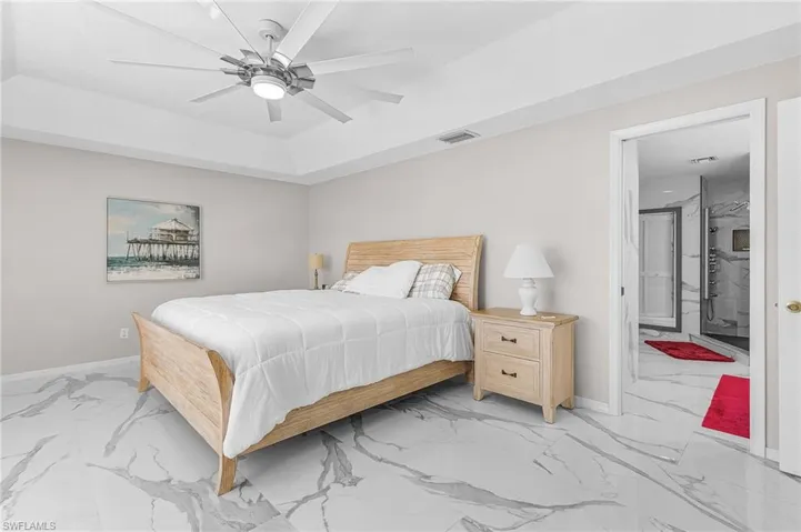 Bedroom featuring marble finish flooring, ceiling fan, a raised ceiling, and connected bathroom