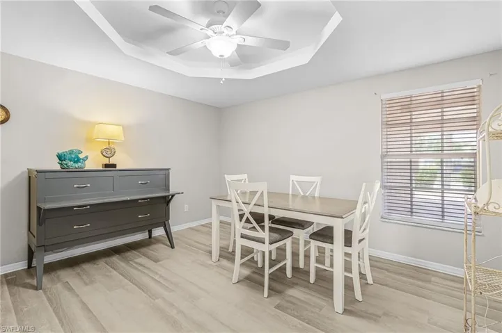 Dining space with a tray ceiling, light wood-type flooring, and ceiling fan