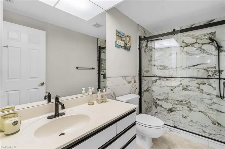 Bathroom with a marble finish shower, vanity, light tile patterned floors, and tile walls