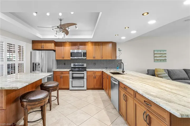 Kitchen featuring a breakfast bar area, brown cabinetry, light stone counters, stainless steel appliances, and recessed lighting