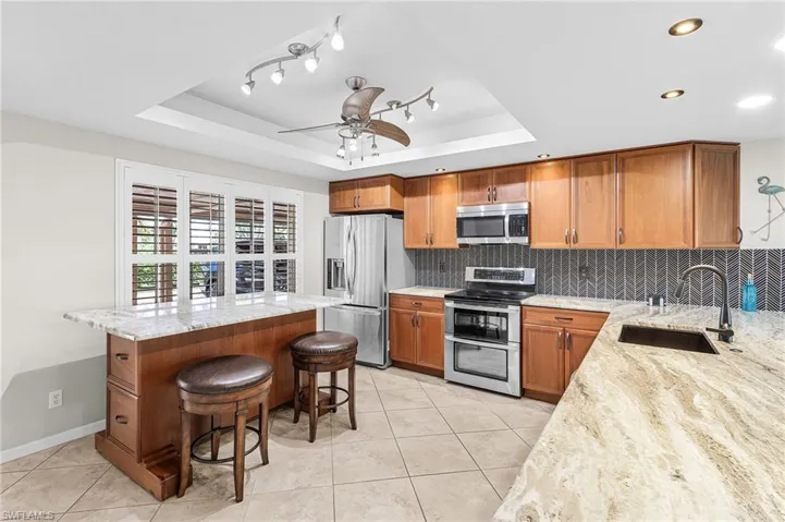 Kitchen featuring brown cabinetry, light stone countertops, stainless steel appliances, and a raised ceiling