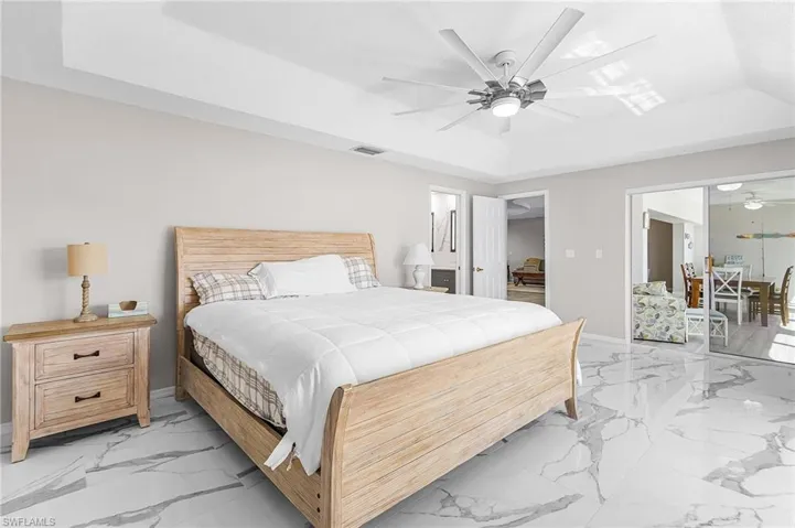 Bedroom with a tray ceiling, light marble finish flooring, and a ceiling fan