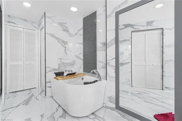 Full bathroom with a closet, stone wall, a soaking tub, marble tiled floors, and recessed lighting