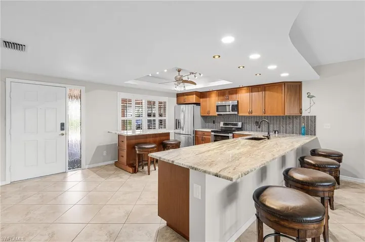 Kitchen with a breakfast bar area, brown cabinets, a peninsula, a tray ceiling, and recessed lighting