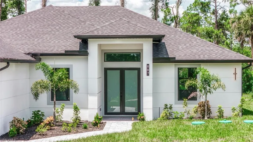Entrance to property with a shingled roof, stucco siding, french doors, and a yard