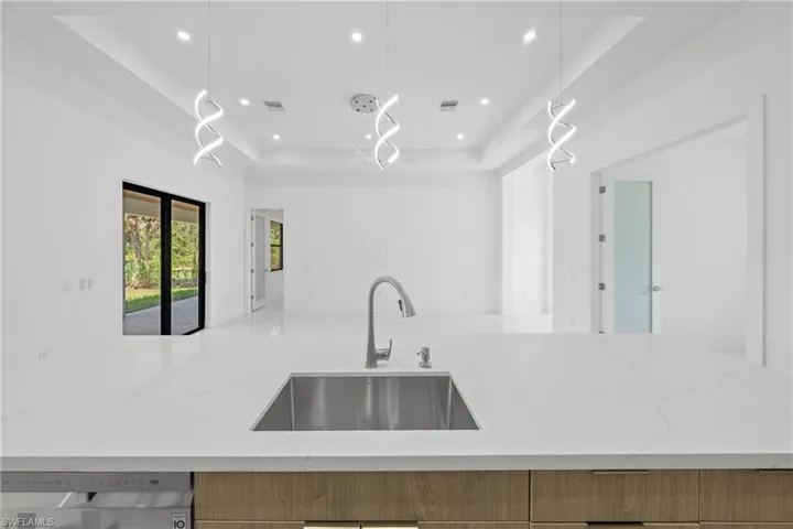 Kitchen featuring a tray ceiling, light stone countertops, pendant lighting, recessed lighting, and open floor plan