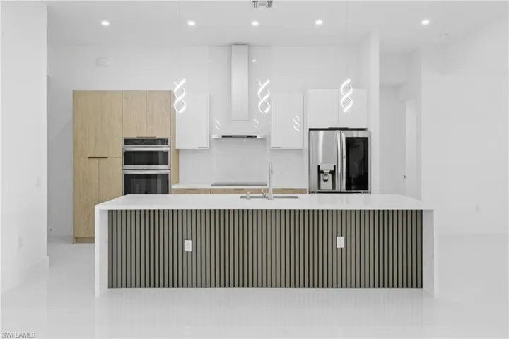 Kitchen with modern cabinets, light stone countertops, recessed lighting, white cabinetry, and a large island with sink