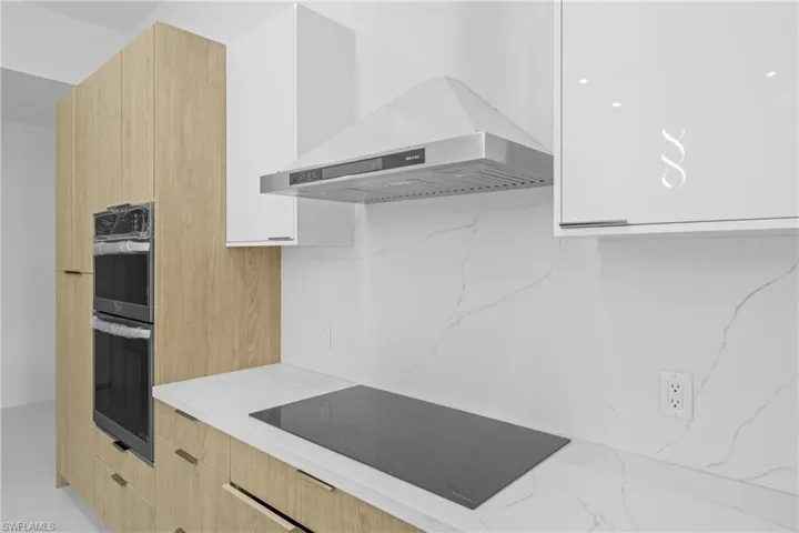 Kitchen with modern cabinets, light brown cabinets, black electric cooktop, light stone countertops, and double oven