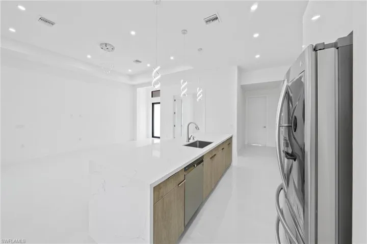 Kitchen featuring modern cabinets, stainless steel appliances, light stone countertops, hanging light fixtures, and recessed lighting