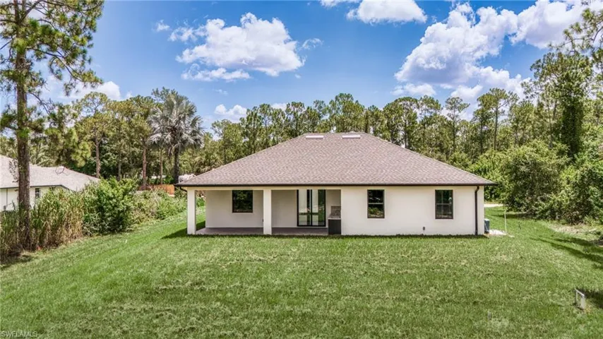 Back of house with stucco siding, a patio, a yard, and a shingled roof