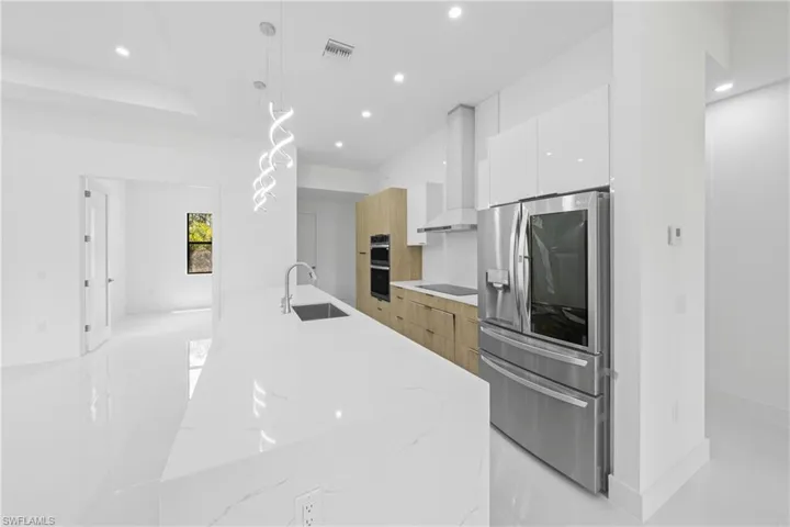 Kitchen featuring light stone counters, modern cabinets, stainless steel refrigerator with ice dispenser, pendant lighting, and recessed lighting