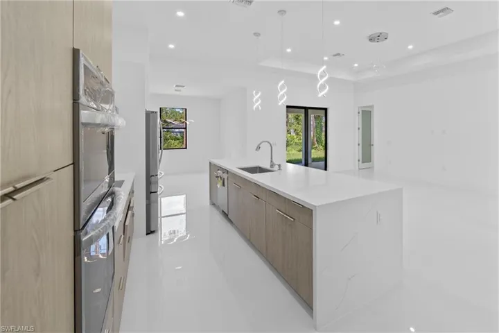Kitchen with modern cabinets, light stone countertops, appliances with stainless steel finishes, pendant lighting, and open floor plan