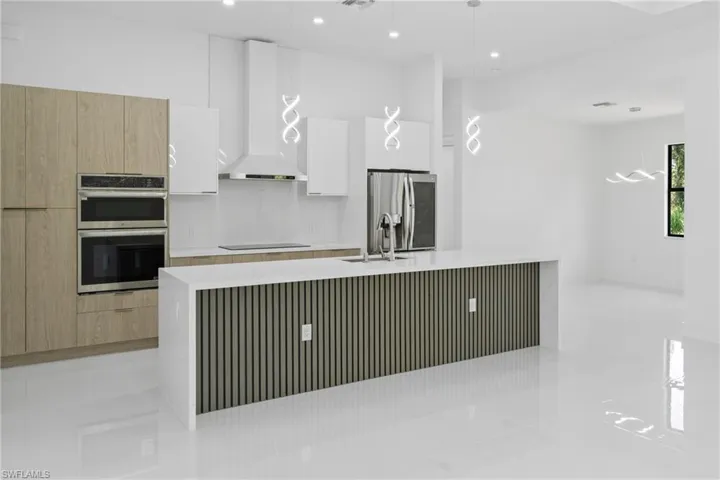 Kitchen featuring modern cabinets, light stone countertops, white cabinets, wall chimney range hood, and stainless steel appliances