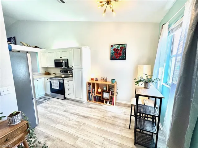 Kitchen with stainless steel appliances, white cabinetry, vaulted ceiling, and light hardwood / wood-style flooring