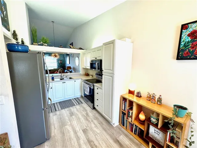 Kitchen with appliances with stainless steel finishes, lofted ceiling, sink, kitchen peninsula, and light wood-type flooring
