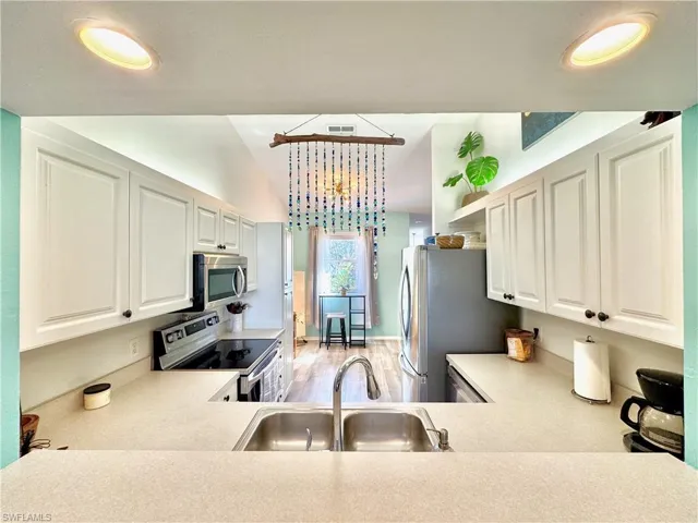 Kitchen with stainless steel appliances, sink, light hardwood / wood-style flooring, and white cabinets