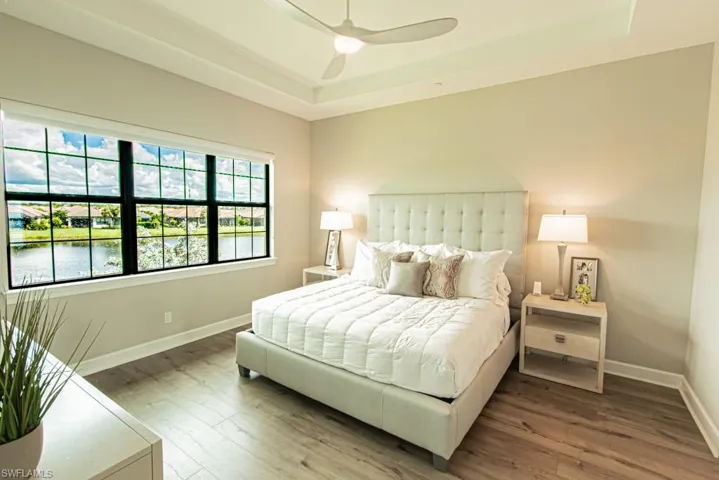 Bedroom featuring a raised ceiling, wood finished floors, a ceiling fan, and a water view