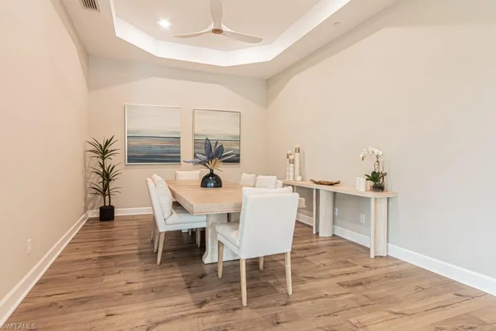 Dining area featuring a raised ceiling, light wood finished floors, and ceiling fan