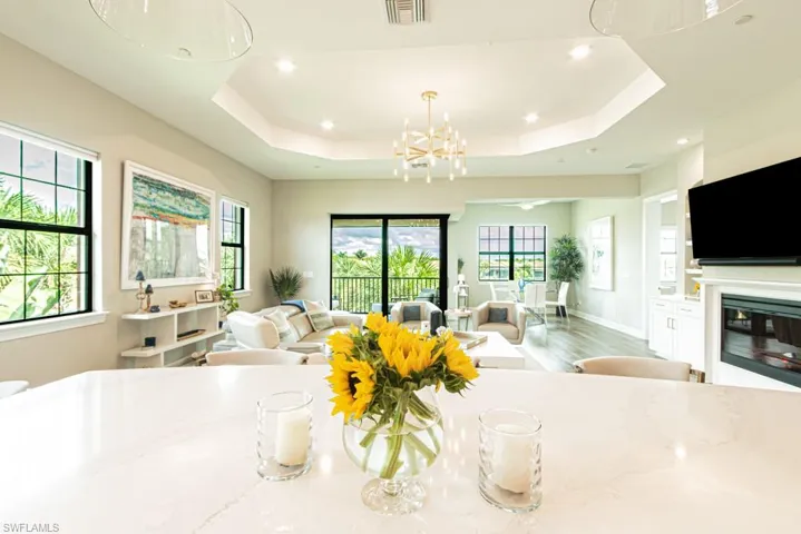 Living room with a glass covered fireplace, wood finished floors, a chandelier, recessed lighting, and a tray ceiling