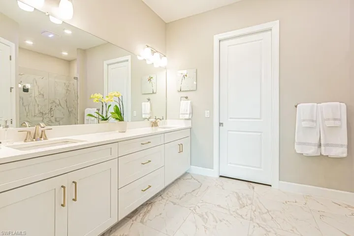 Full bath with light marble finish floors, a marble finish shower, and double vanity
