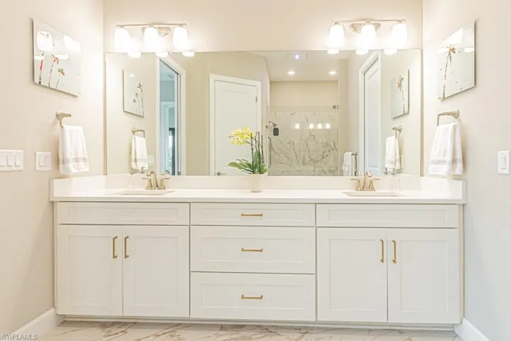 Full bathroom with double vanity, light marble finish floors, and a marble finish shower