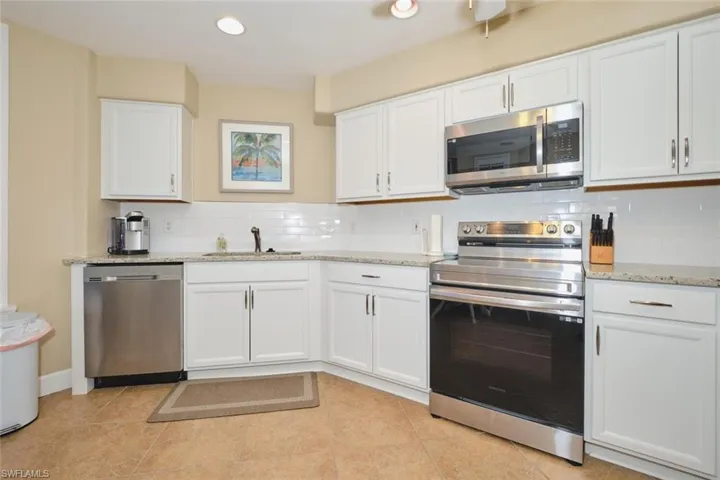 Kitchen with stainless steel appliances, white cabinets, light stone counters, and recessed lighting