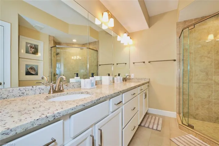 Bathroom with a shower stall, double vanity, and light tile patterned floors