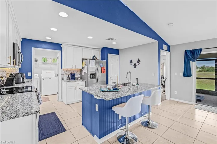 Kitchen featuring light tile patterned floors, a breakfast bar area, white cabinetry, stainless steel appliances, and vaulted ceiling