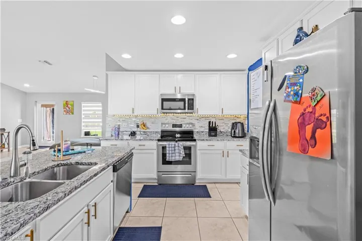 Kitchen featuring appliances with stainless steel finishes, white cabinetry, light stone counters, light tile patterned floors, and recessed lighting