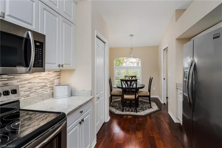 Kitchen and dining space featuring wood-finish flooring, white cabinetry, a stainless steel microwave, and light-toned countertops