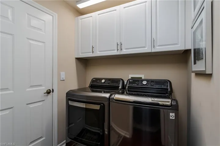 Laundry area featuring overhead white shaker-style cabinetry with brushed nickel hardware, a white paneled door, and neutral wall tones