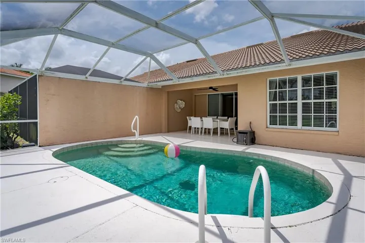 Screened-in patio featuring a kidney-shaped pool with integrated steps, tile roofline, and an expansive concrete deck