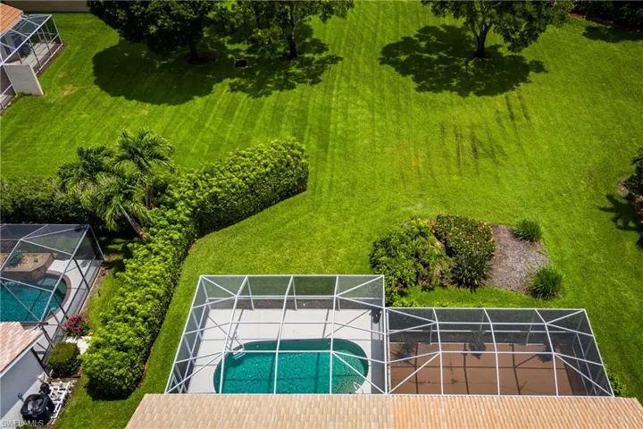 Screened-in pool and patio area featuring a freeform swimming pool with a concrete deck, bordered by mature hedges